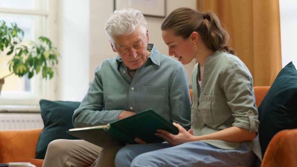 Elderly man and young woman sharing a moment while looking at a photo album together, fostering connection and reminiscing.