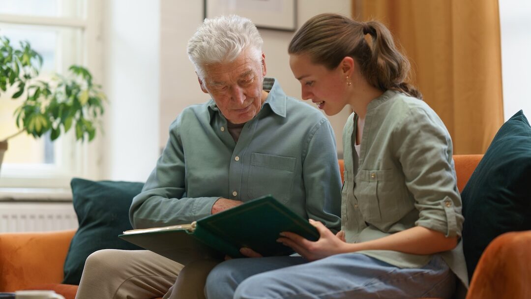 Elderly man and young woman sharing a moment while looking at a photo album together, fostering connection and reminiscing.