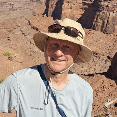 Smiling man in a wide-brimmed hat and sunglasses, standing in a rocky canyon landscape, enjoying a sunny day outdoors.